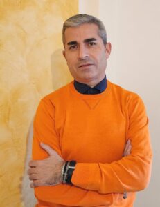 Foto-ritratto dello scrittore Sebastian Ruggiero, autore del Fato Racconta (Edizioni Erickson) con un maglione arancione e le braccia conserte